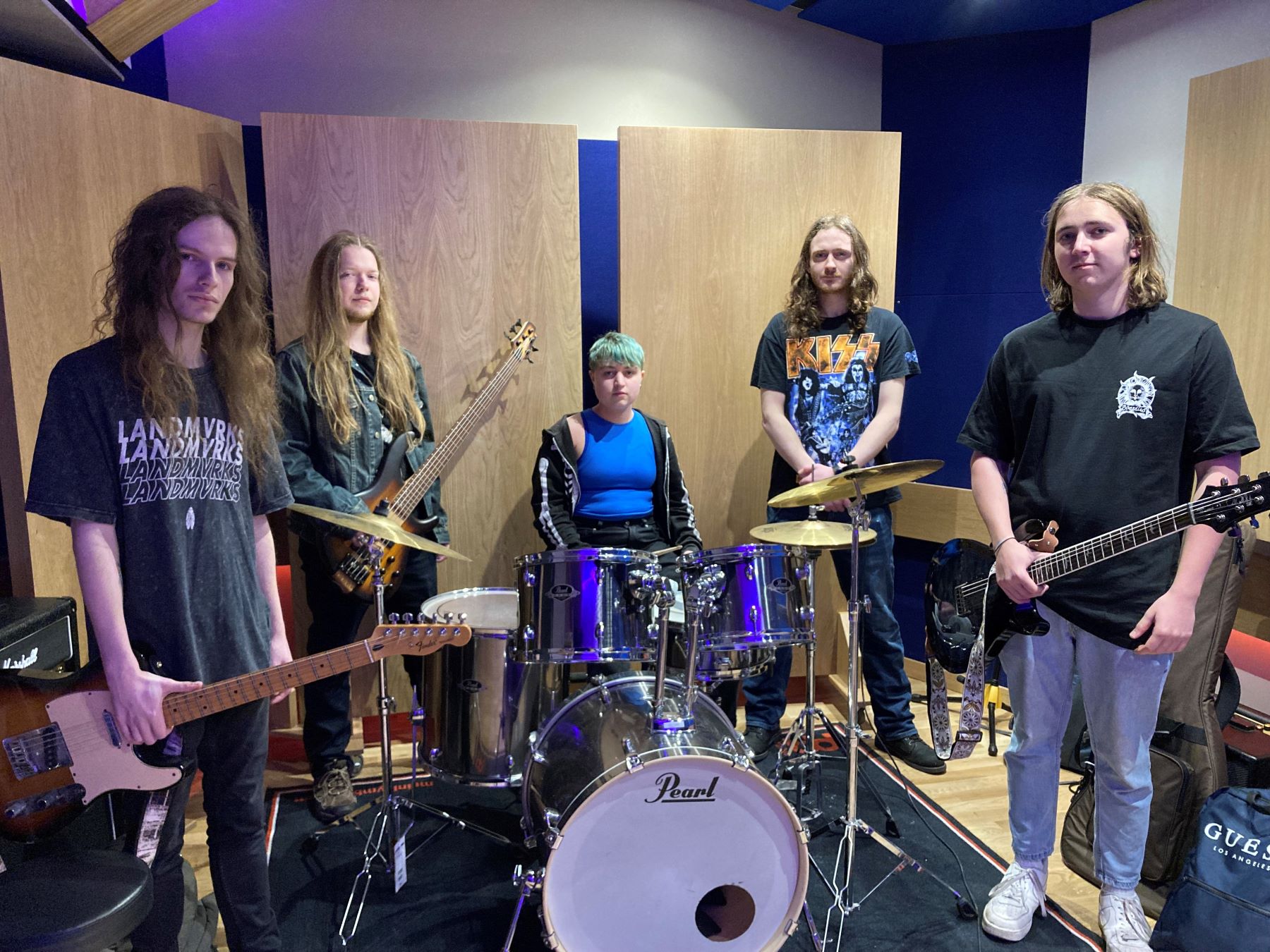 Five piece rock band in studio. Four long-haired young man and girl drummer with short hair