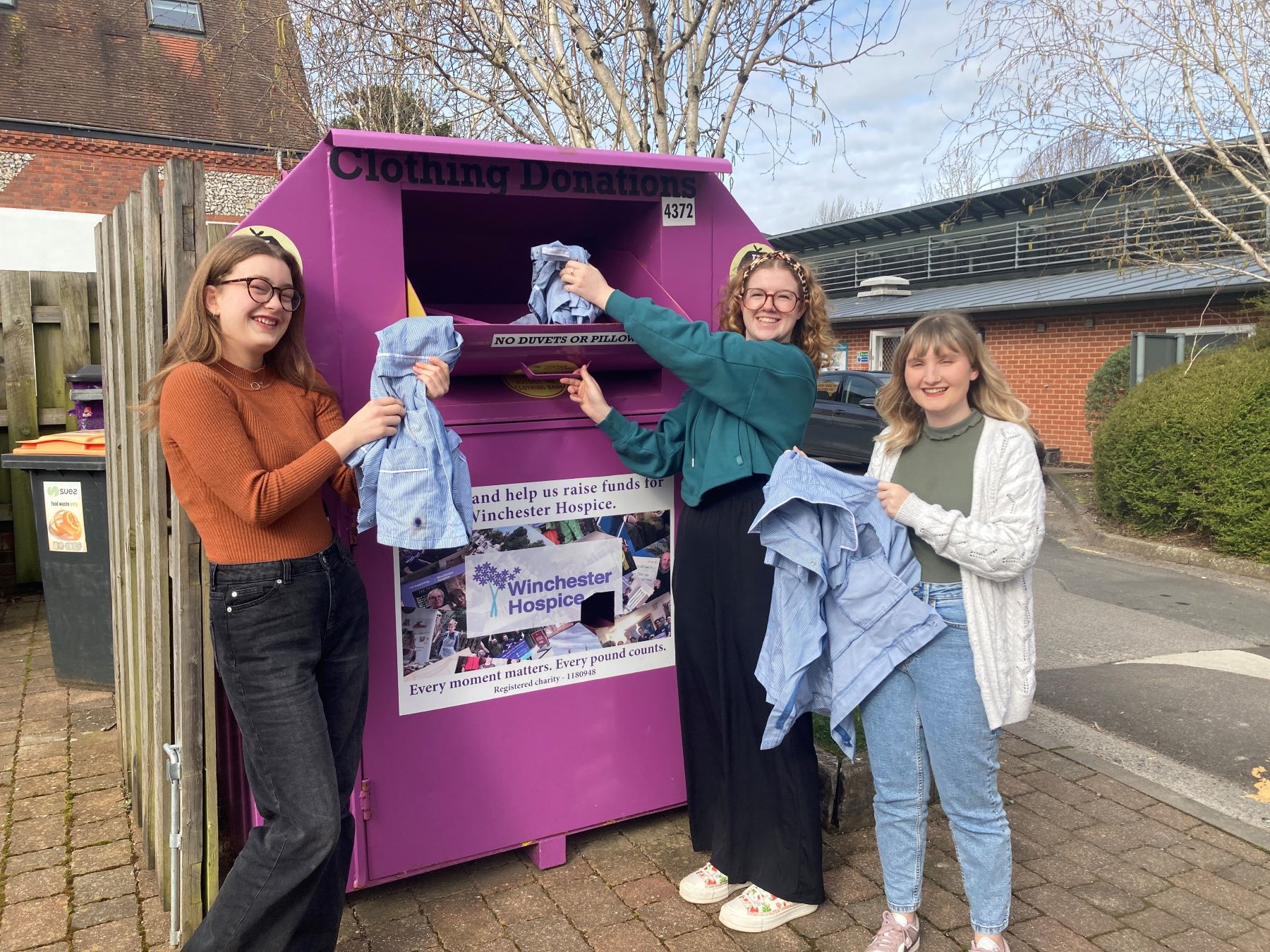 Three young women putting clothes into recycling bin