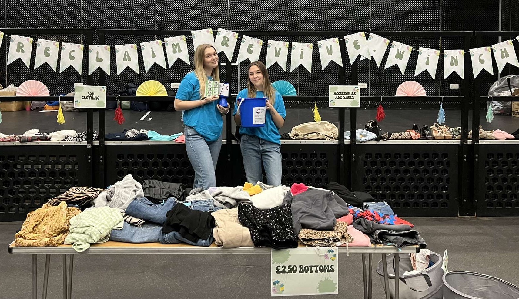 Two young women standing front of bunting at a clothes swap