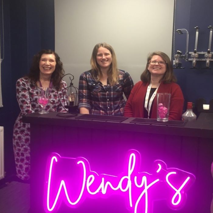 three women behind bar bearing pink neon letters Wendy's