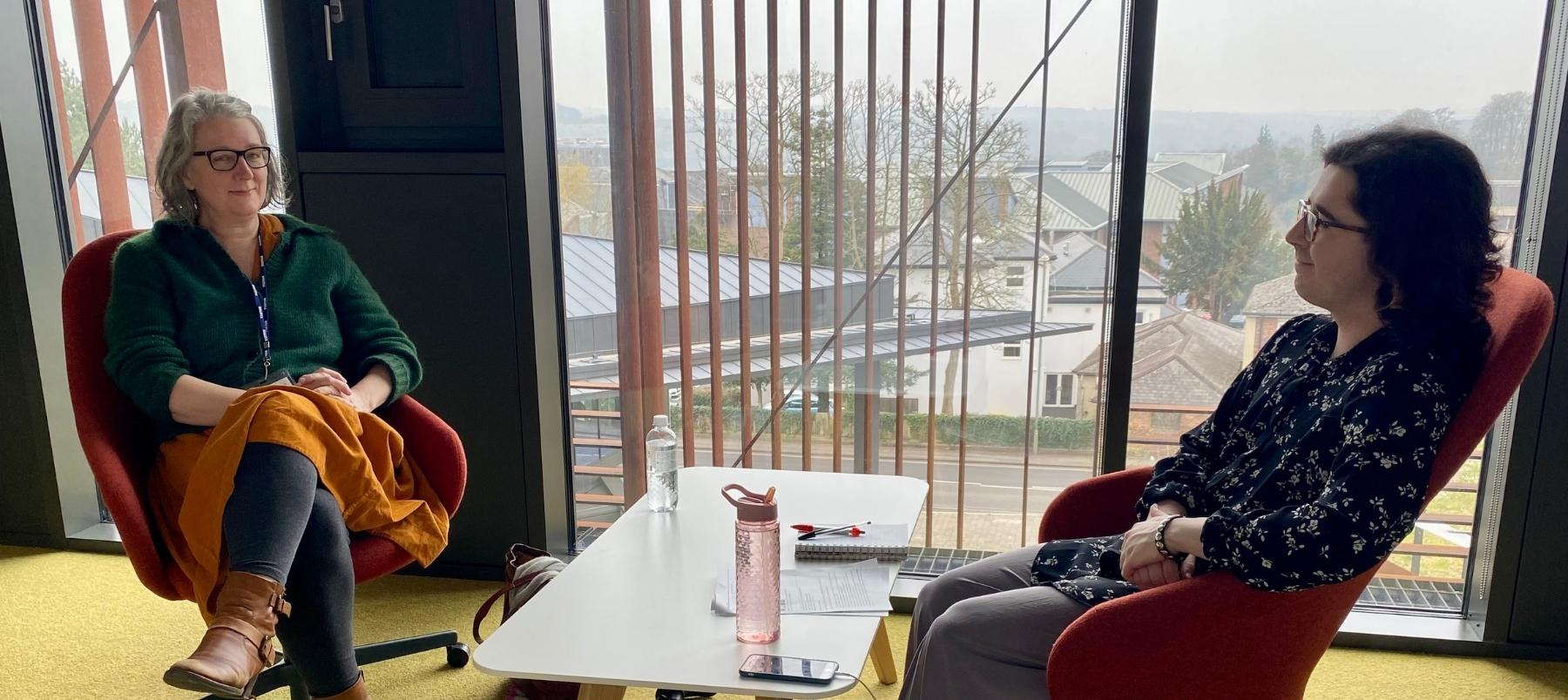 Alumna Clare Fuller and student Eden Irving sitting across a table in conversation in the West Downs Centre