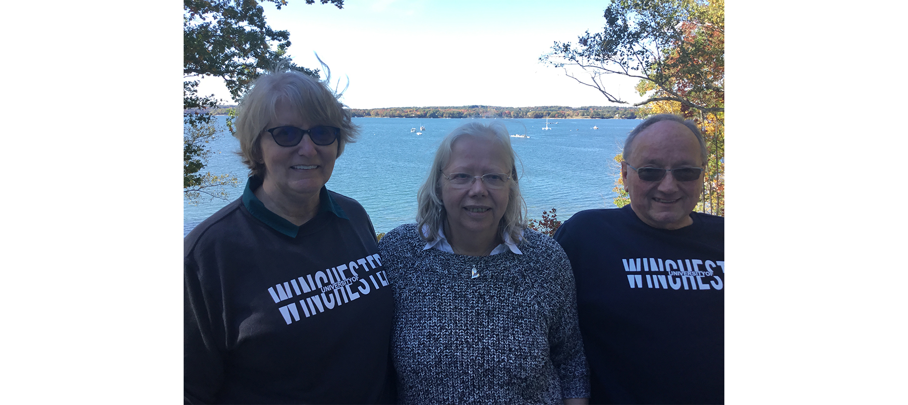 Three people standing with lake in background