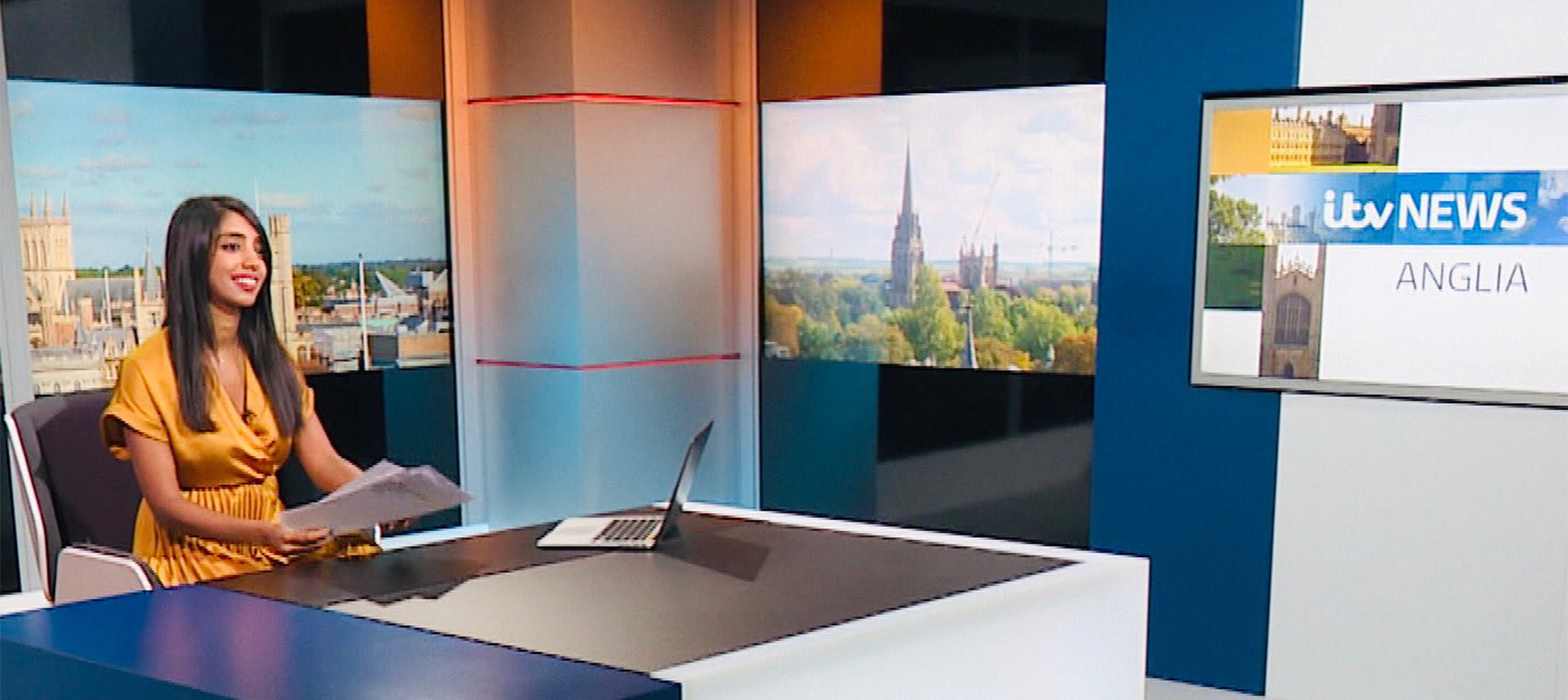 A woman sitting at a desk in front of TV screens