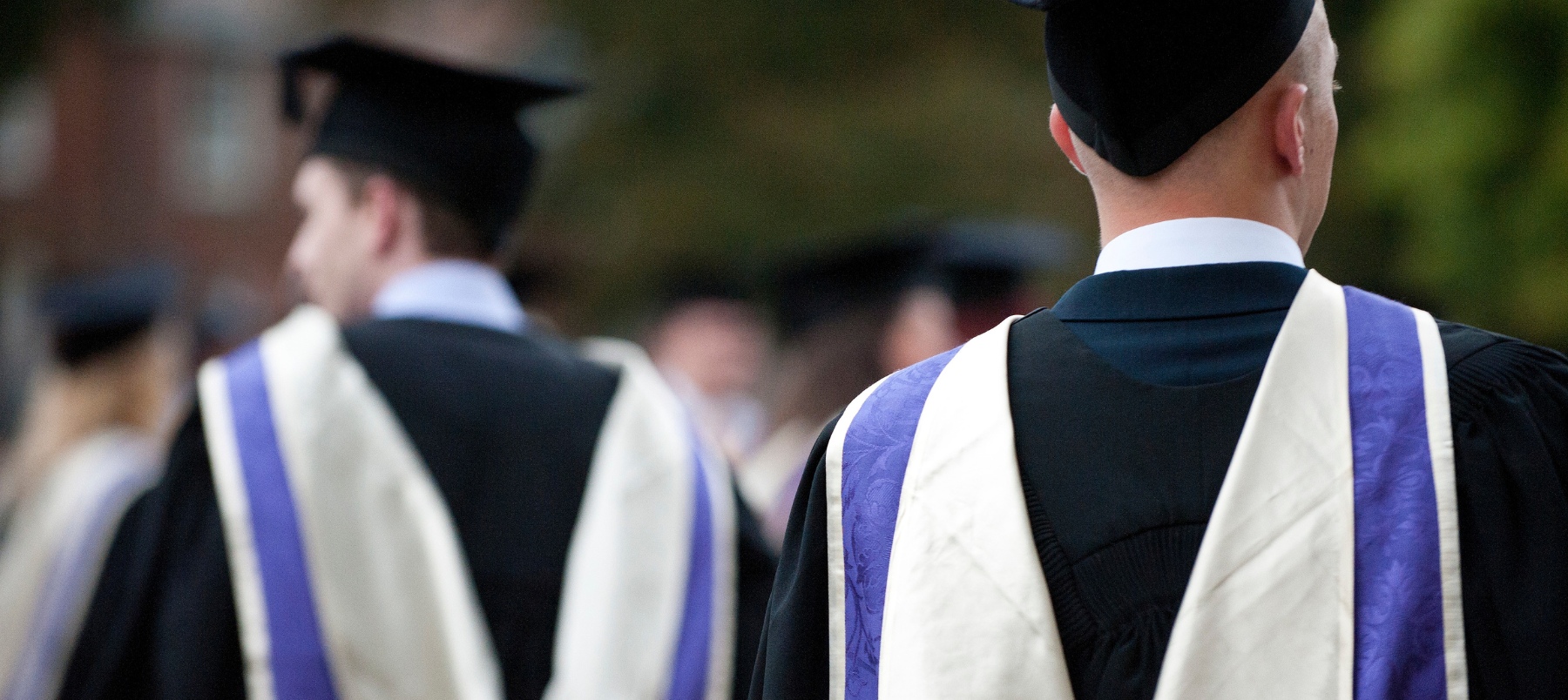 two male students walking through the Cathedral grounds wearing graduation gowns