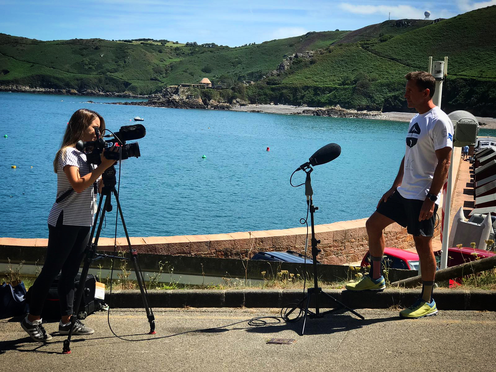 Two people with filming equipment at a coastal scene