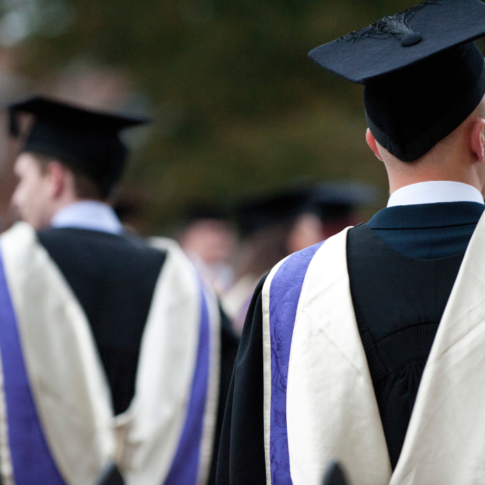 two male students walking through the Cathedral grounds wearing graduation gowns