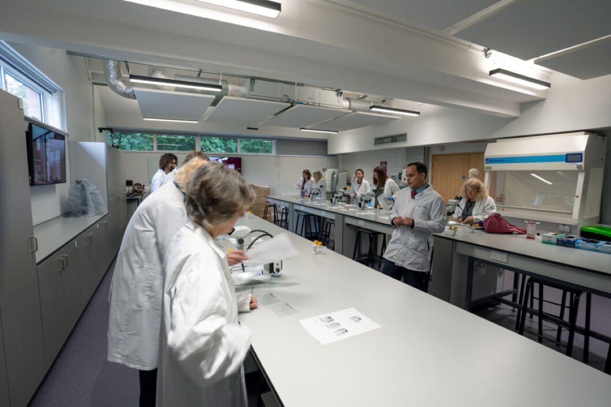 People in white lab coats standing around a lab bench