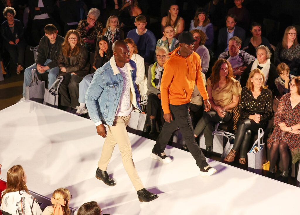 Two male models walk down catwalk at fashion show
