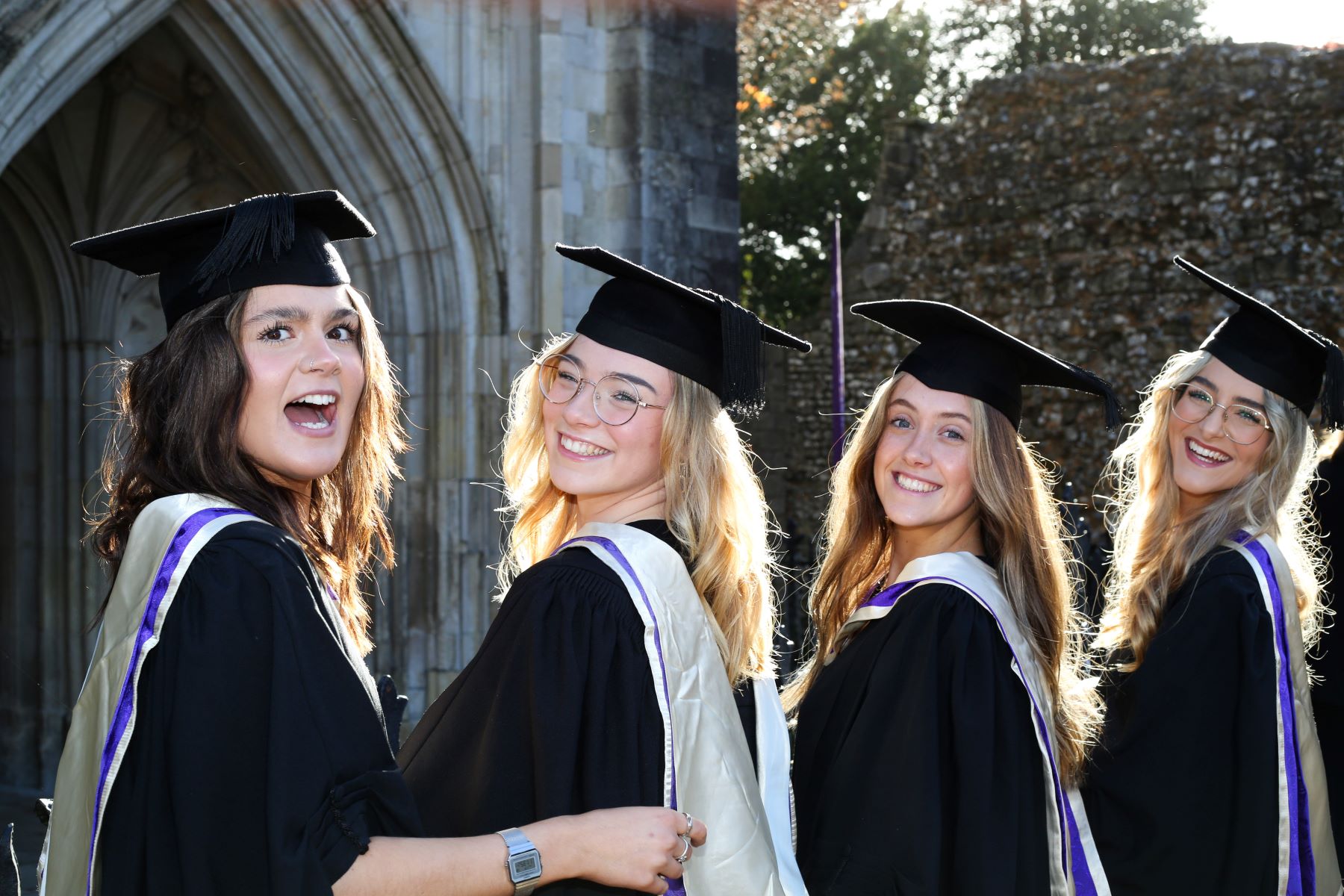Three graduate girls in robes looking over their shoulders