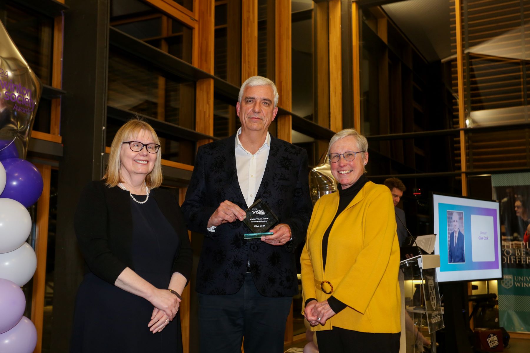 Man with glass trophy flanked by two women