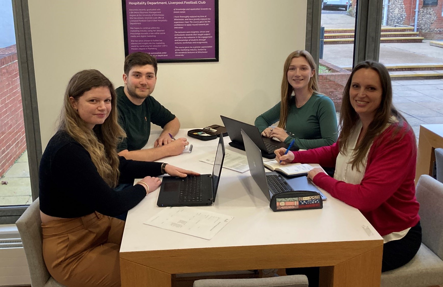 Three young women and a young man sat around table with laptops