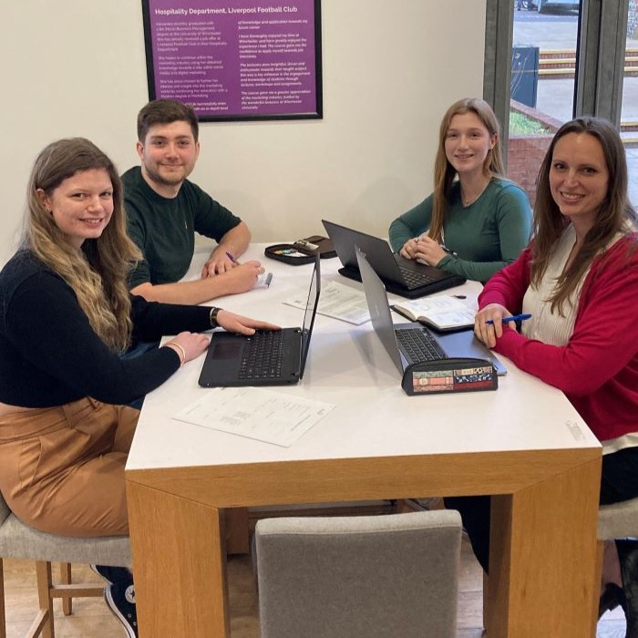 Three young women and a young man sat around a table with laptops