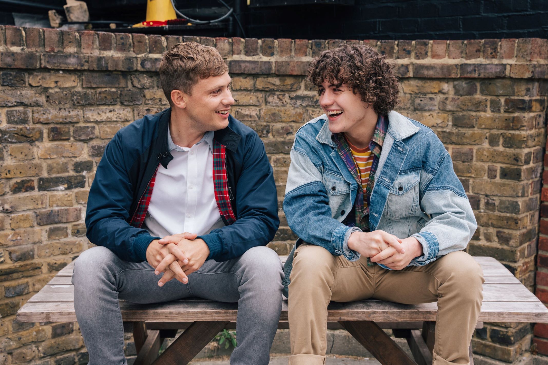 Two young men seated on bench laughing