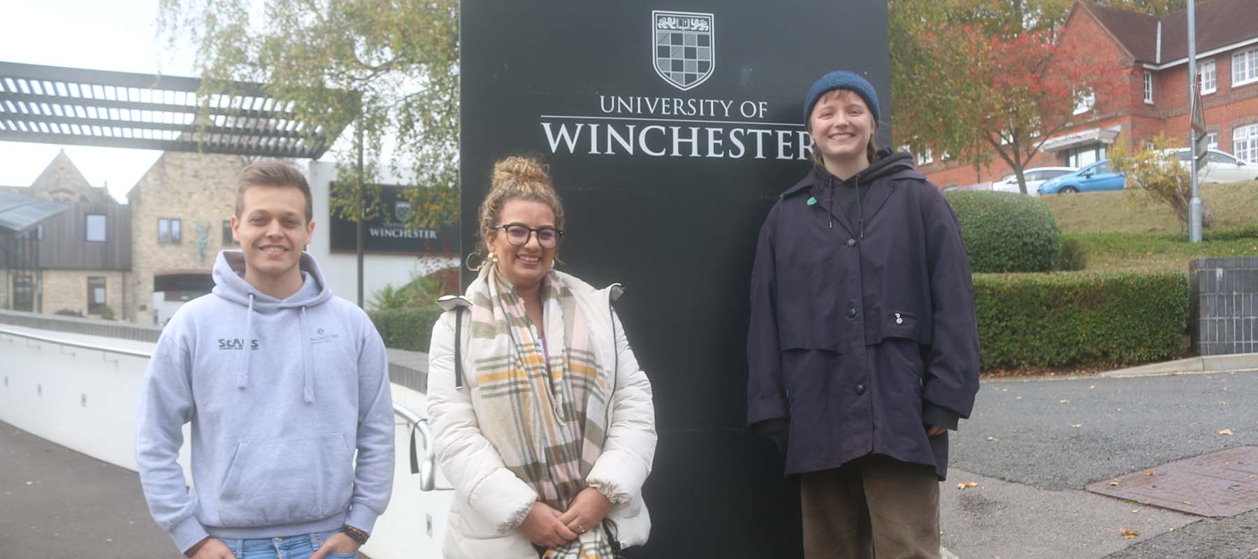 Three students standing at the main entrance to the University