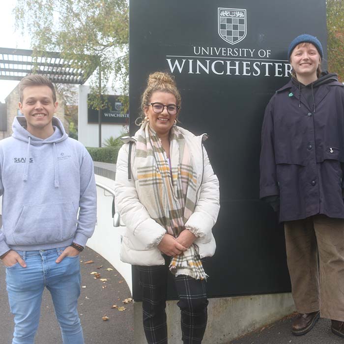 Three students standing at the main entrance to the University