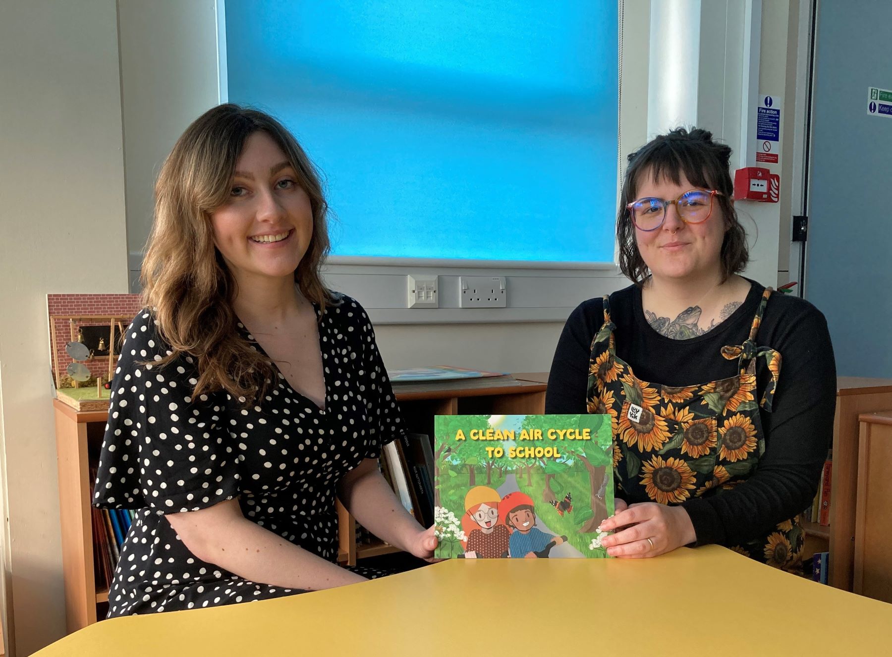 Two young women sitting at desk with children's picture book