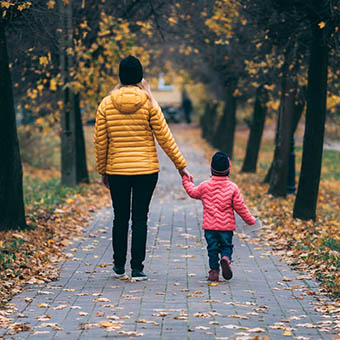 Mother and young child holding hands walking along a path in autumn landscape