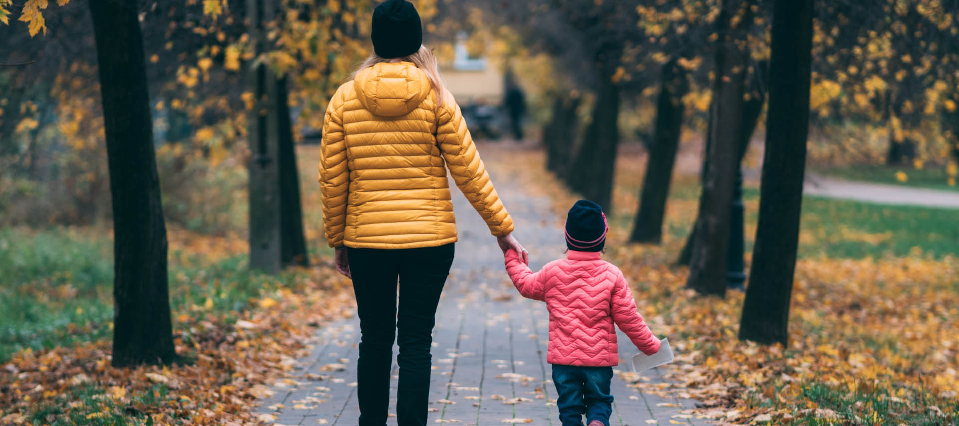 Mother and young child holding hands walking along a path in autumn landscape