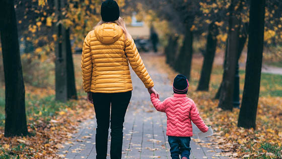 Mother and young child holding hands walking along a path in autumn landscape