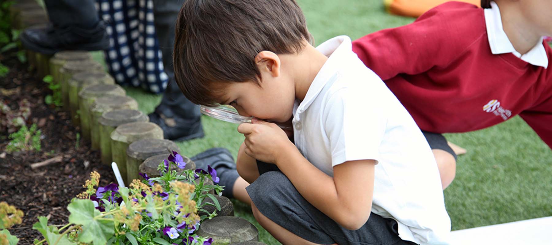 Small boy crouching and looking through a magnifying glass at a plant