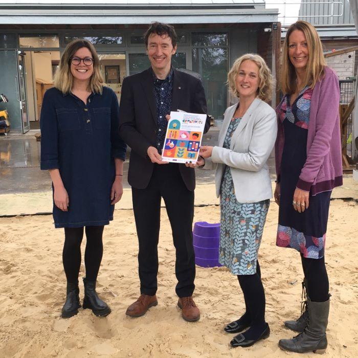 four people stood holding a book and smiling