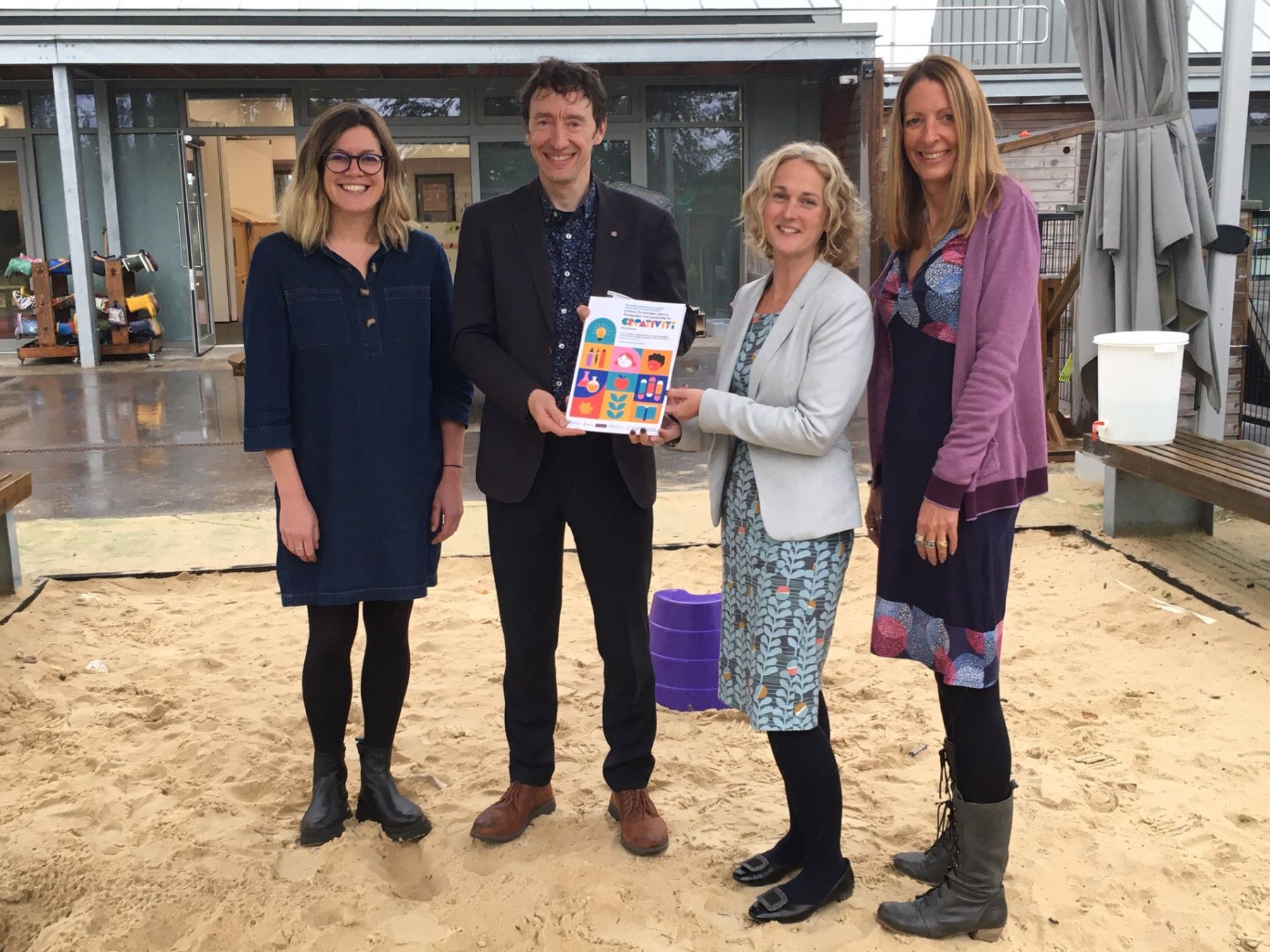 Three women and man in school sandpit with new report