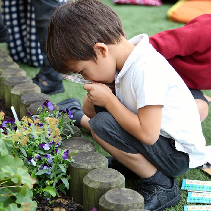 Small boy crouching and looking through a magnifying glass at a plant