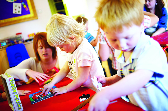 primary school children playing in a classroom helped by a teacher