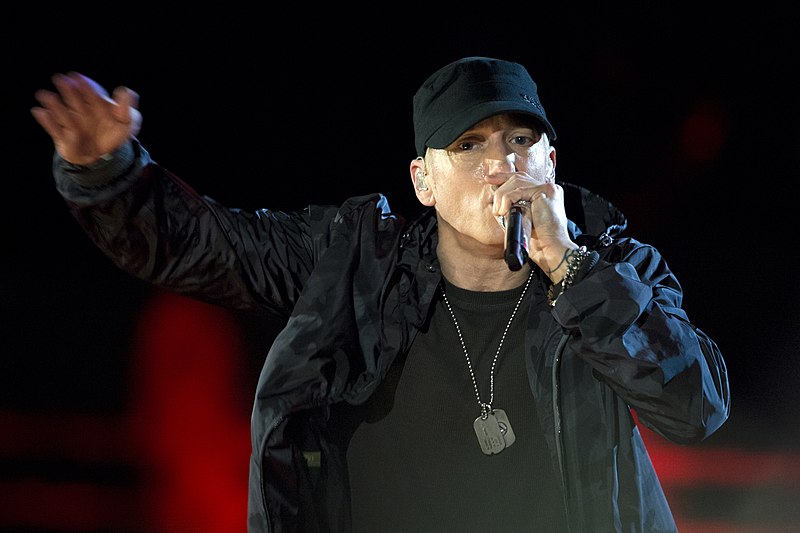 rapper Eminem on stage with mic. Wearing dark baseball cap.