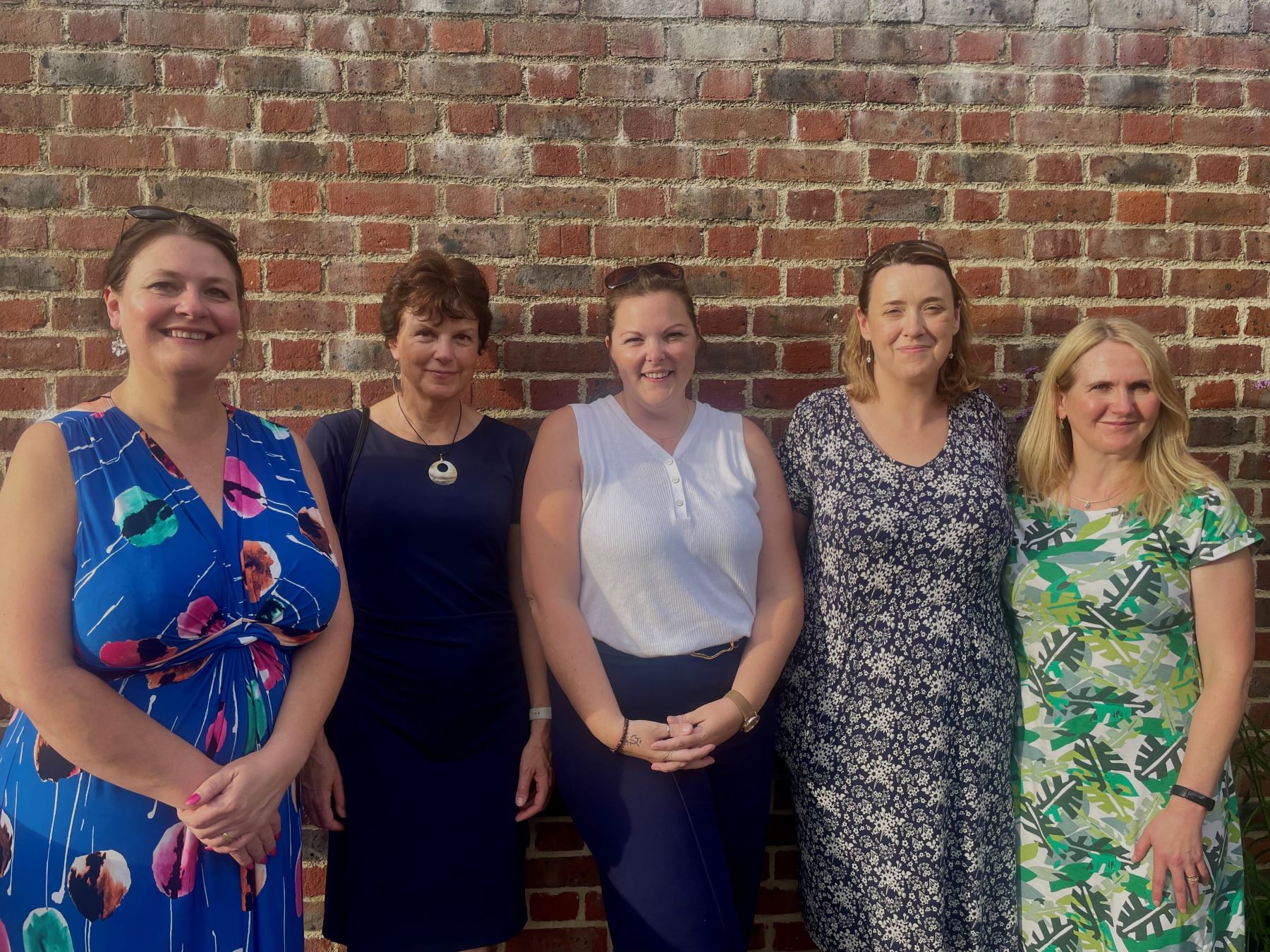 Five women standing against brick wall