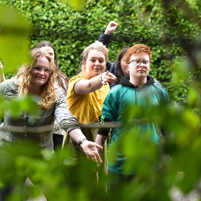 Two female students looking through a fence covered in foliage