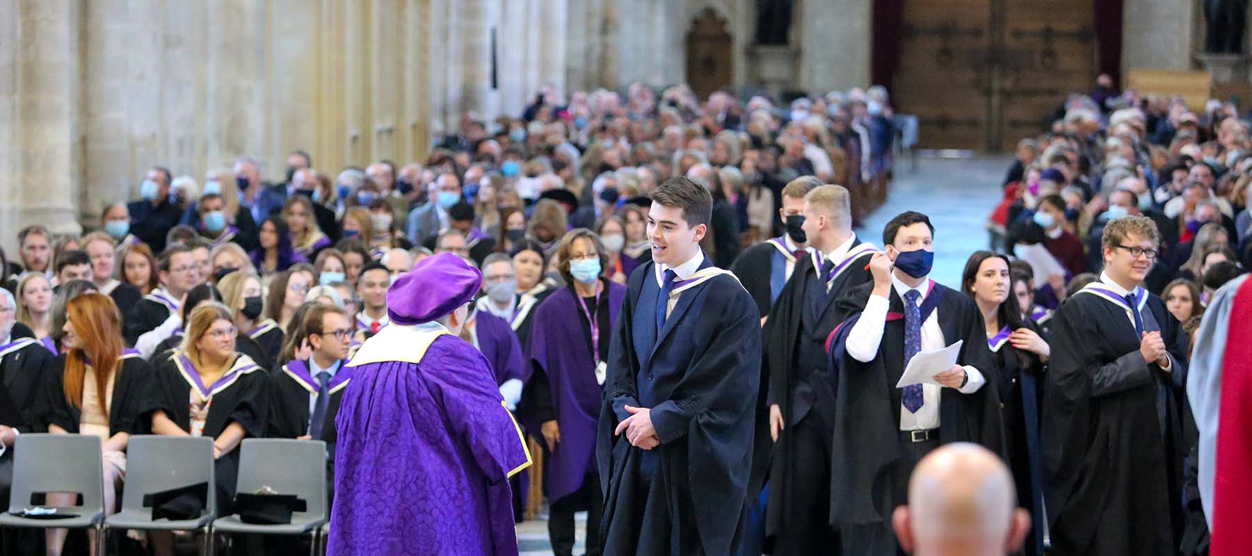 Three students in graduation robes standing with their arms around each other