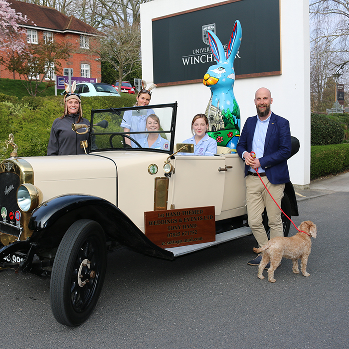 Giant hare sculpture in back of vontage car with group of people