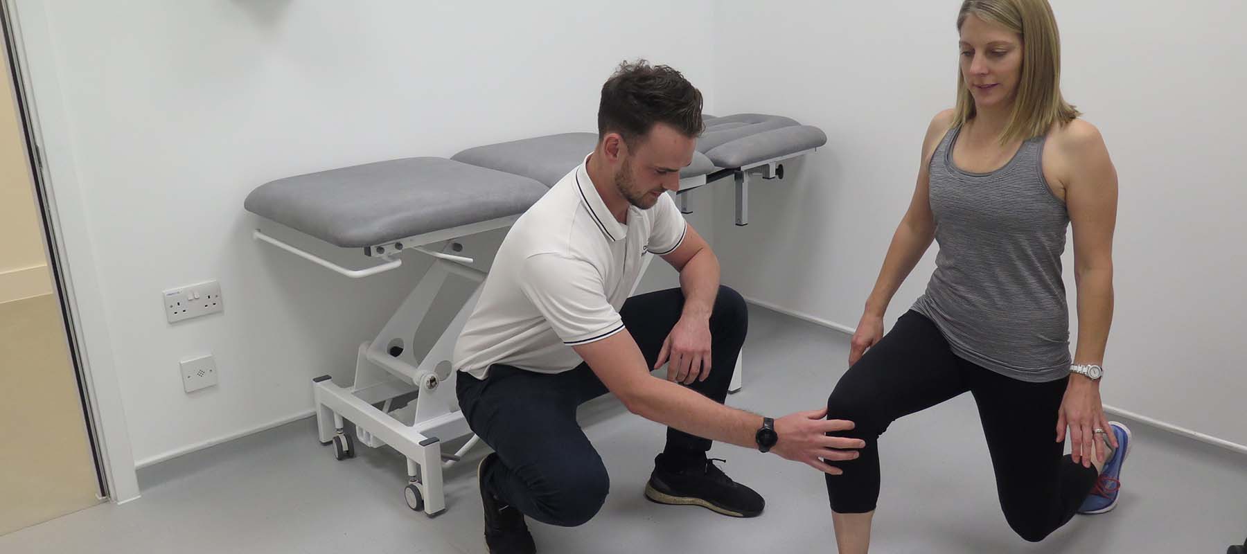 Physiotherapist supports knee of female patient doing a forward leg lunge