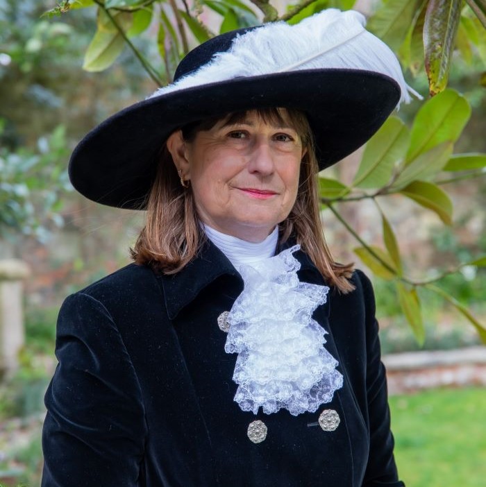 Woman in black robes with white frilly shirtfront and wide brimmed hat with white feather