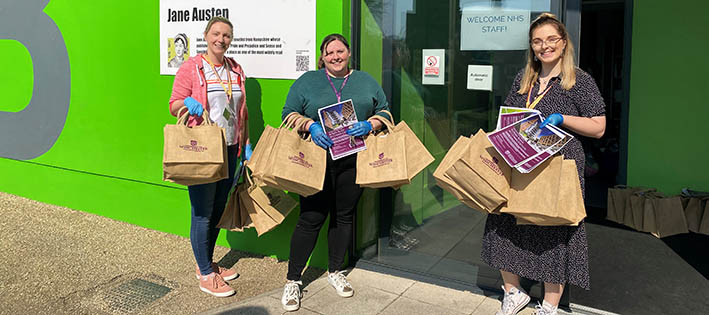 Three female staff with welcome bags standing outside halls of residence