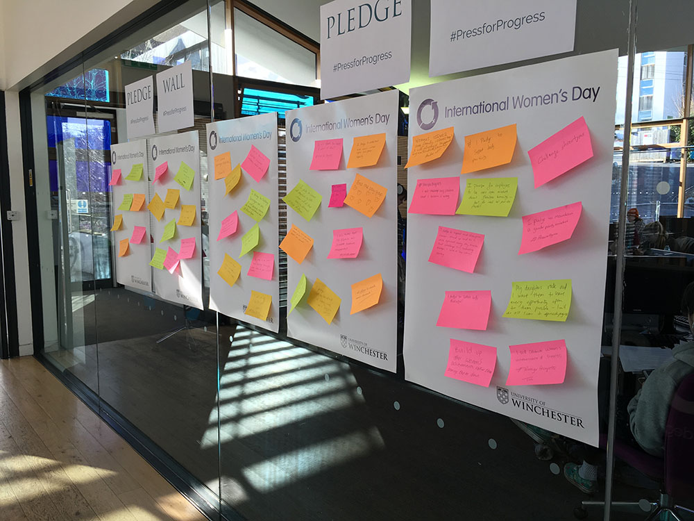 Post it notes with written pledges stuck to glass wall along a corridor