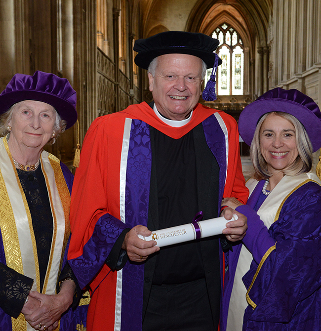 Three people stood at a graduation cermony