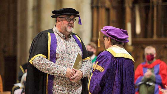 Jock McKenzie in graduation robes talking to David Suchet