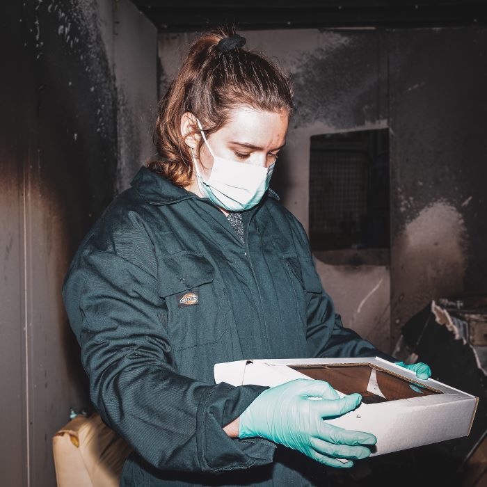 Girl on overalls and face mask carrying a tray at blackened fire scene