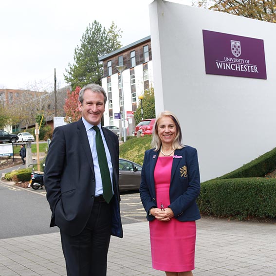 Man in suit and woman in pink dress stand at entrance to University