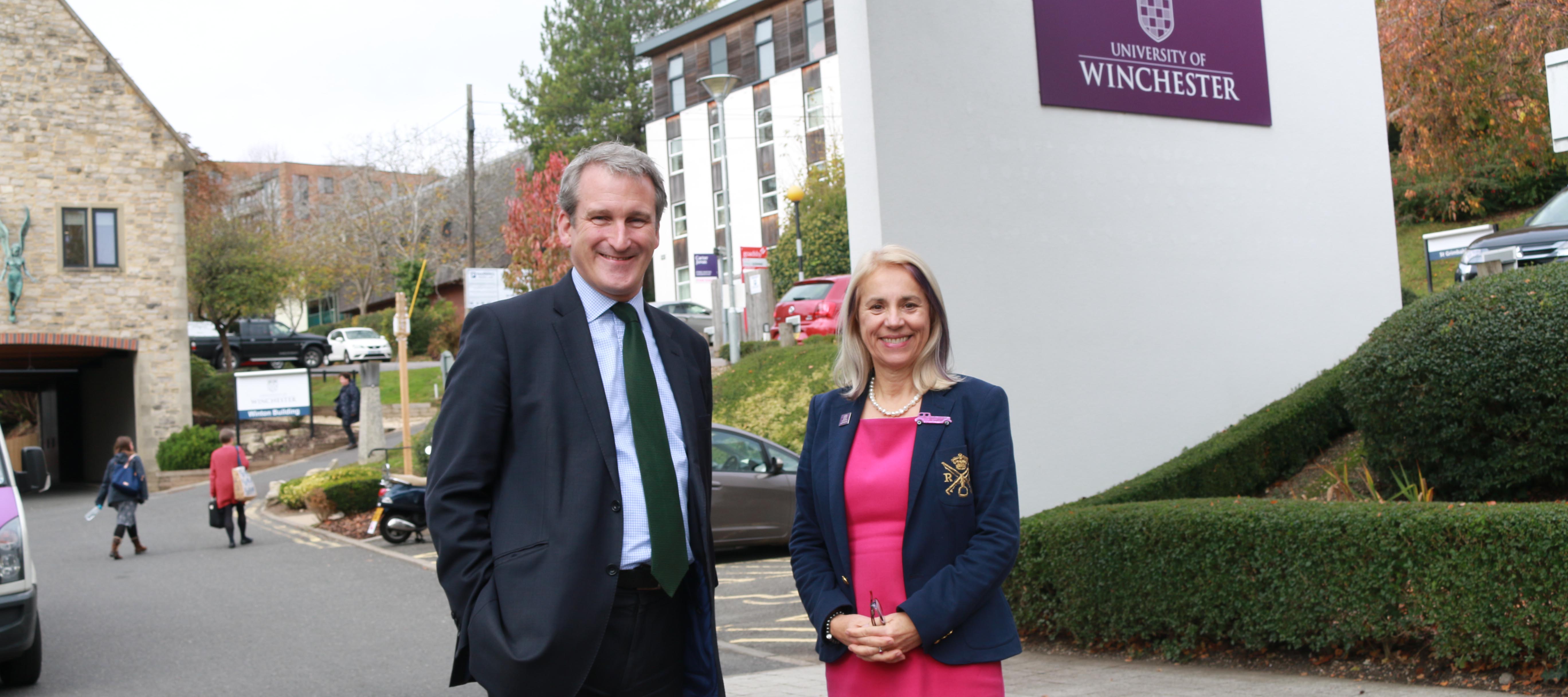 Man in suit and woman in pink dress stand at entrance to University