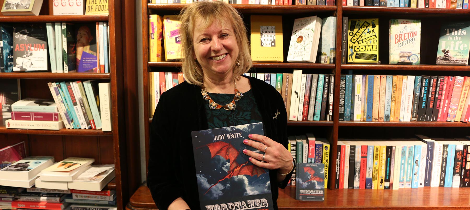 Woman in black dress holding a book standing in front of bookcase