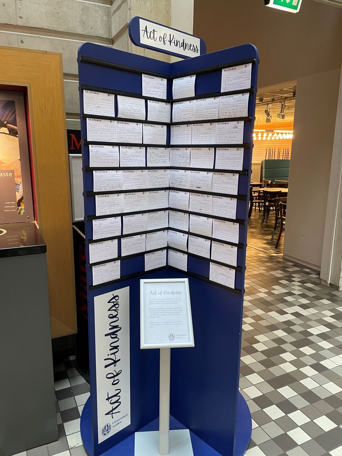 Blue board with white cards pinned to it beneath sign saying Acts of Kindness