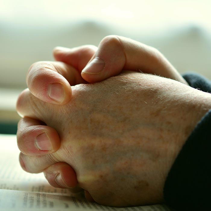 Hands clutched in prayer over an open bible