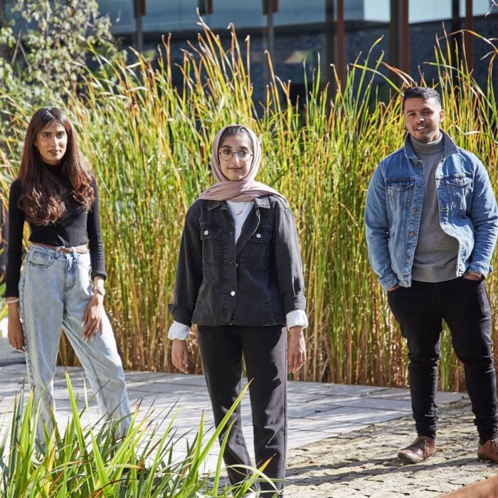 Three students, two young women and a young man, standing in front of tall grass