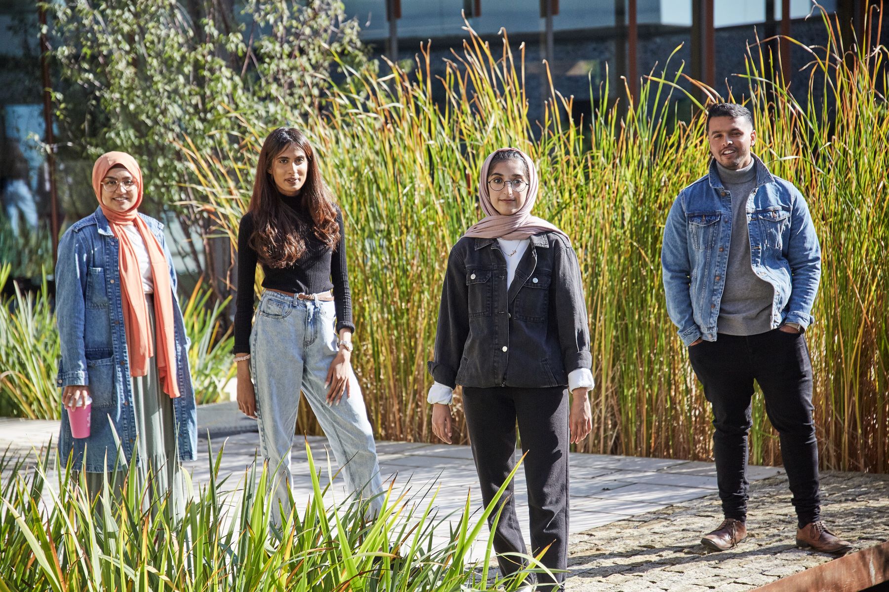 Four students, threee femal one male, standing in front of long grass