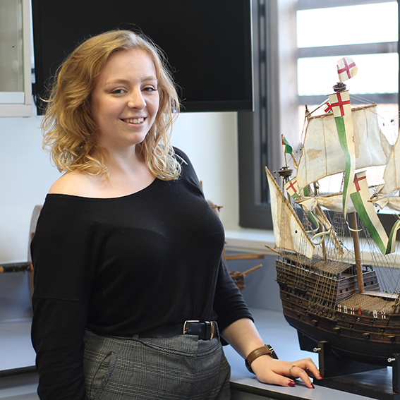 Young woman standing next to a model of a ship with sails