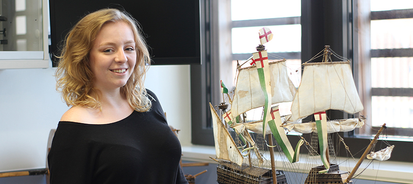 Young woman standing next to a model of a ship with sails