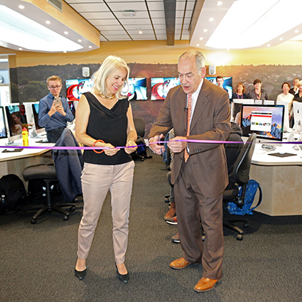 Man and woman cut ceremonial ribbon together in newsroom